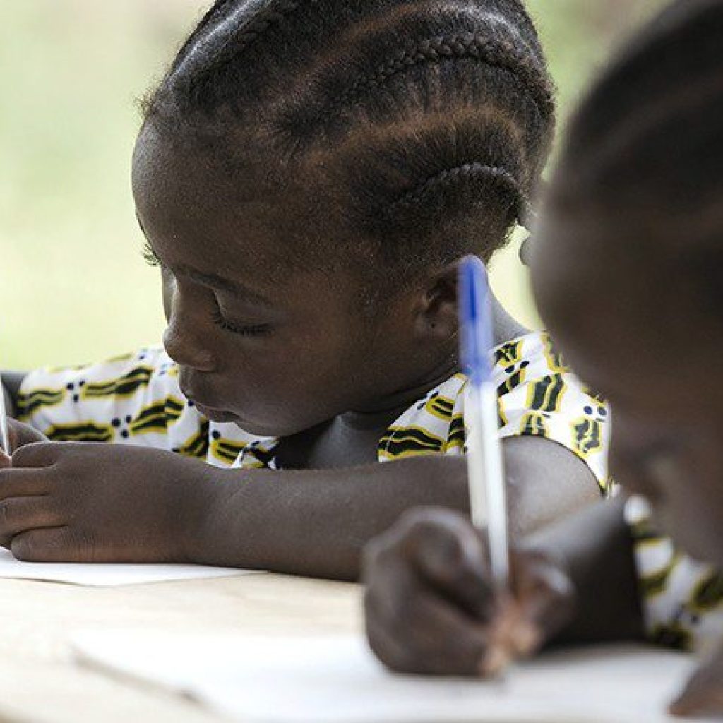 Gorgeous black African ethnicity students writing their essay in an African school in Bamako, Mali. They're holding blue pens to write down their homework whilst sitting in their desk.
